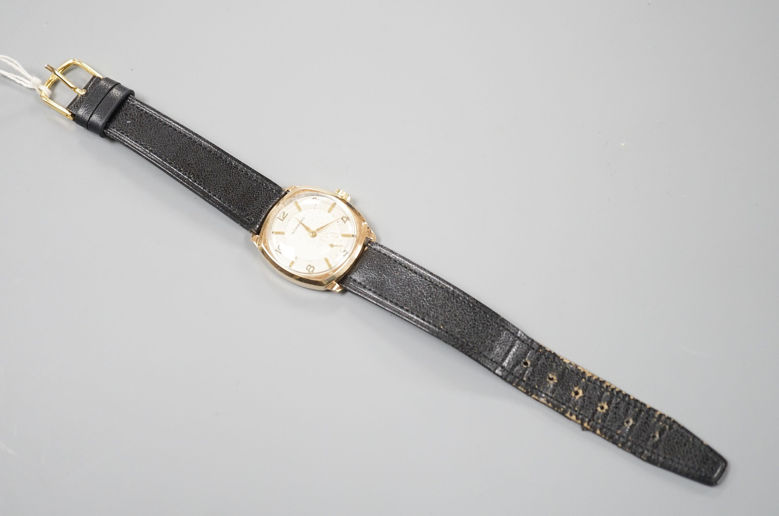 A gentleman's 9ct. gold wristwatch by Garrard in cushion case, silvered dial, baton and Roman numerals, Swiss 16 jewel movement, c.1957 inscription to back, black leather strap, cased diameter, 30mm, gross 24 grams.